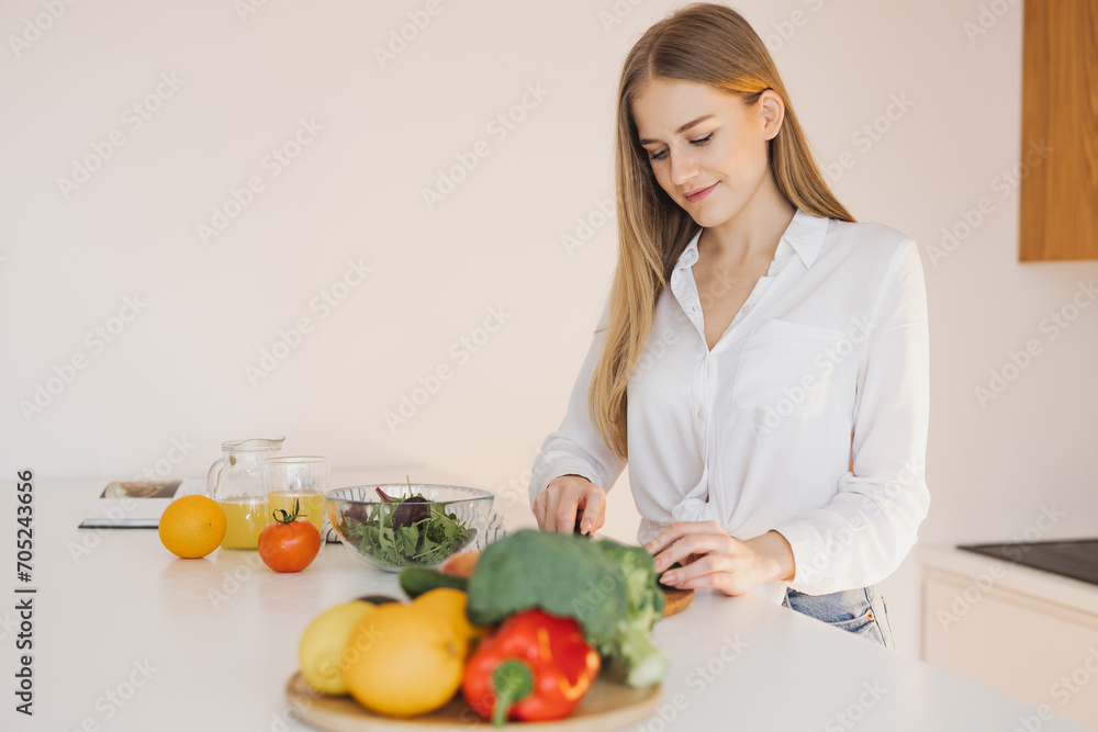 A happy cute blonde woman is preparing a salad in the kitchen