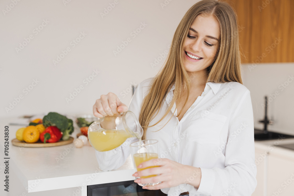 A happy cute blonde woman drinks orange juice in the kitchen A happy cute blonde woman drinks orange juice in the kitchen