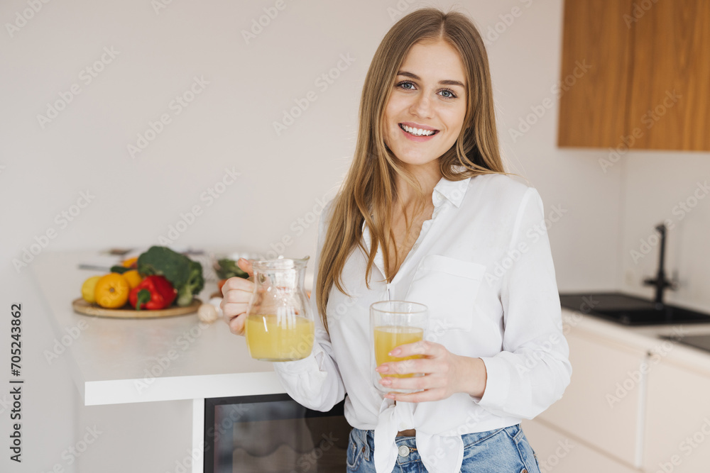 A happy cute blonde woman drinks orange juice in the kitchen A happy cute blonde woman drinks orange juice in the kitchen