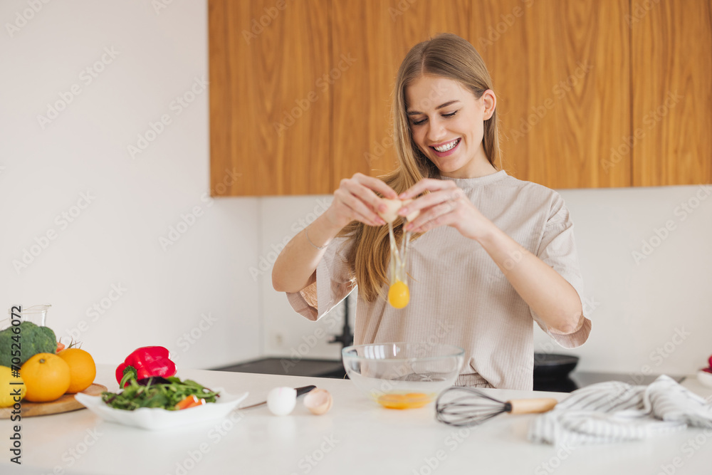 Happy pretty blonde woman in pajamas is preparing breakfast of eggs and fresh vegetables in the kitchen at home. Happy pretty blonde woman in pajamas is preparing breakfast of eggs and fresh vegetables in the kitchen at home.