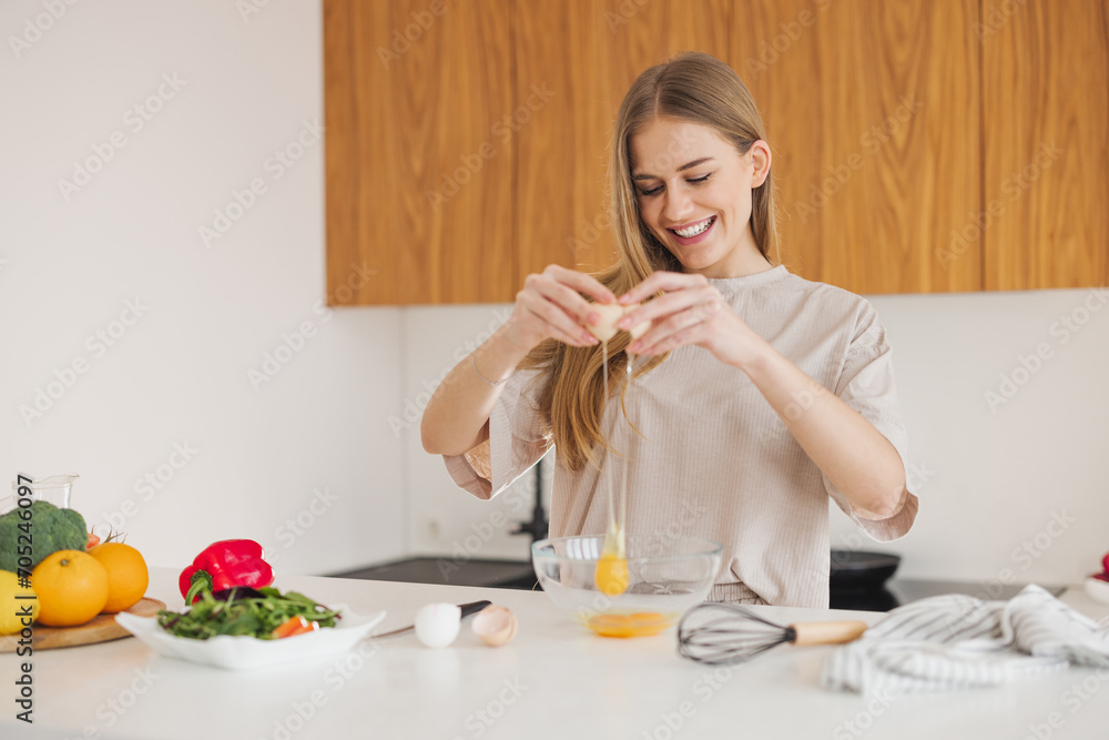 Happy pretty blonde woman in pajamas is preparing breakfast of eggs and fresh vegetables in the kitchen at home. Happy pretty blonde woman in pajamas is preparing breakfast of eggs and fresh vegetables in the kitchen at home.