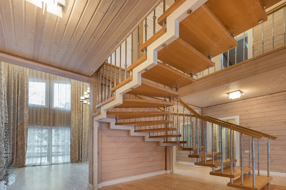 Obraz premium The interior of the living room, decorated with light wood, with beautiful curtains on a .large window. Stairs with wooden steps.