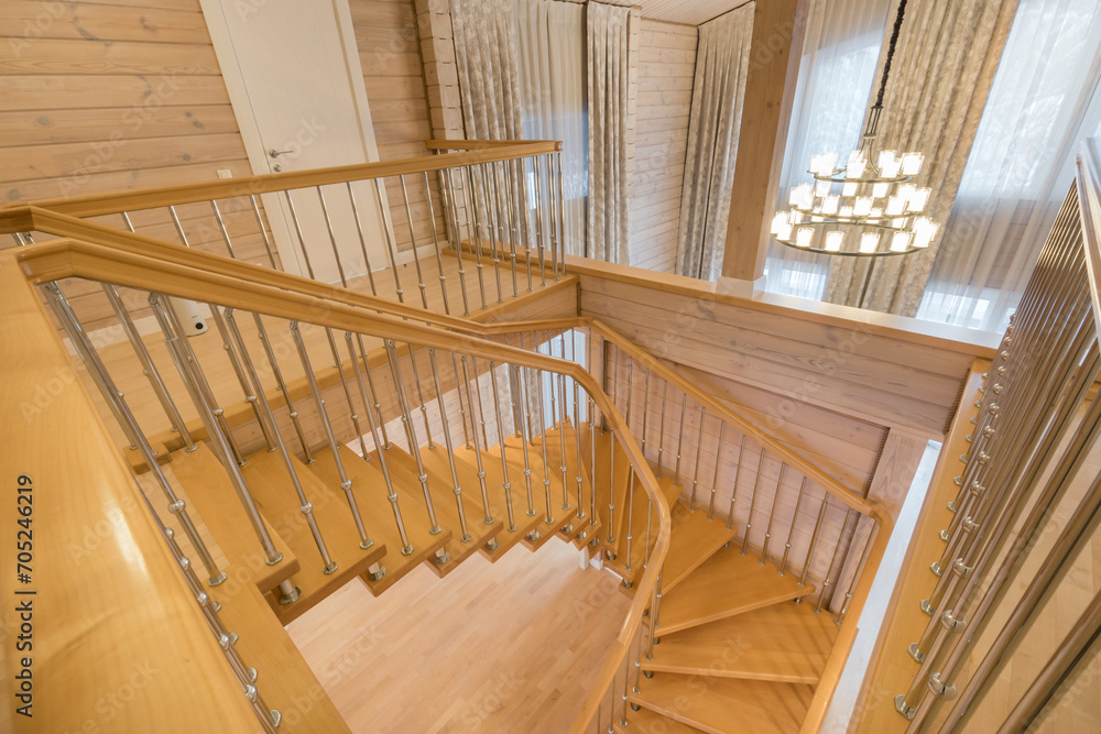 Obraz premium View of the stairs inside the living room of a private house with light wood trim. Large .windows with curtains.