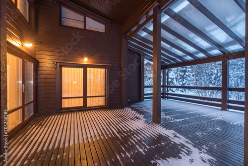 Light from the windows of the wooden house to the terrace under the canopy. Twilight. .Winter landscape. photo