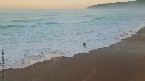 Lonely surfer entering ocean drone shot. Wonderful pastel sky with marine waves