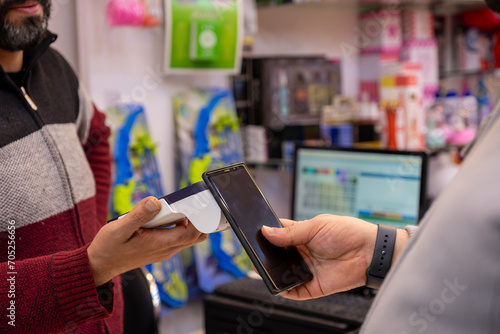 A man makes contactless payments at a bookshop or gift shop using his smartphone , seamlessly utilizing NFC or WiFi technology, without the need for physical touch photo
