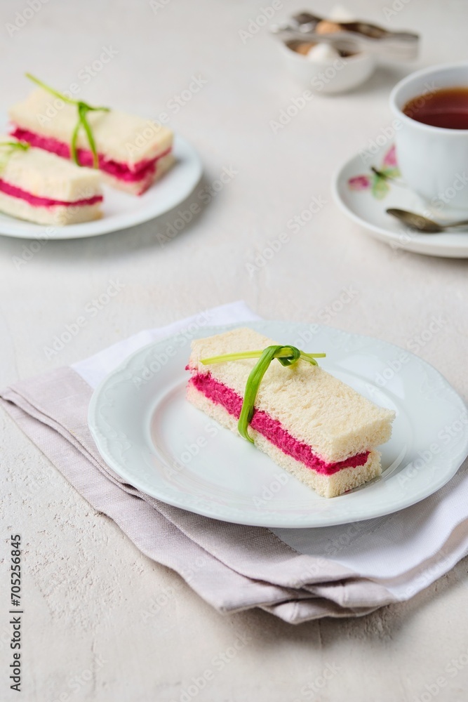 Tea sandwiches on white bread with beetroot hummus on a light ceramic plate on a light concrete background. Sandwiches for tea Tea sandwiches on white bread with beetroot hummus on a light ceramic plate on a light concrete background. Sandwiches for tea