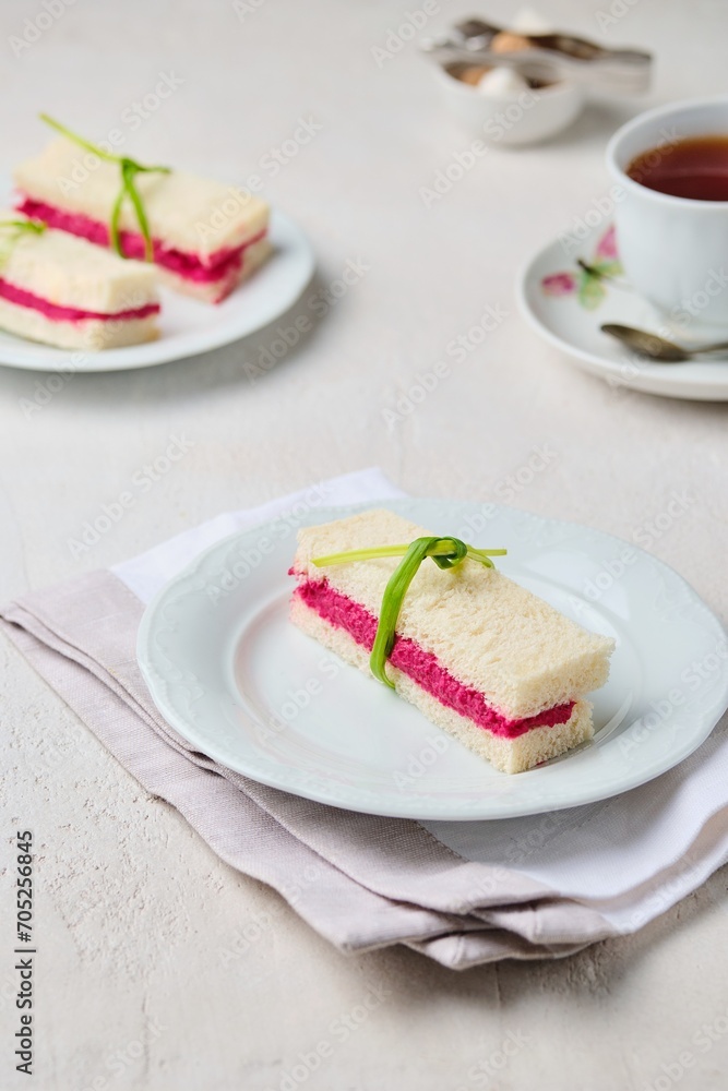 Tea sandwiches on white bread with beetroot hummus on a light ceramic plate on a light concrete background. Sandwiches for tea