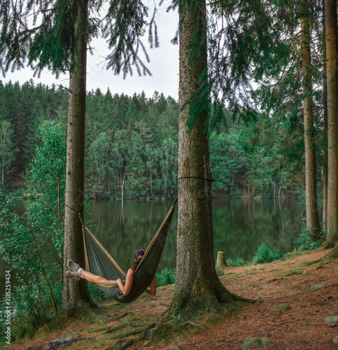 Woman resting in a green hammock by a lake in Swedish forest. Wild camping in Sweden. Klåveröd, Klåverödsdammen, Klåveröd strövområde. Camping site Söderåsens National Park.