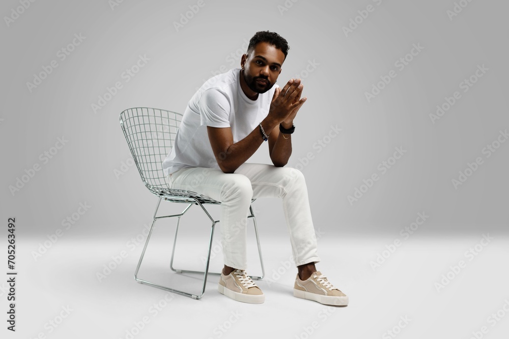 Fototapeta premium Handsome young african american guy sitting on stool, posing in studio - isolated
