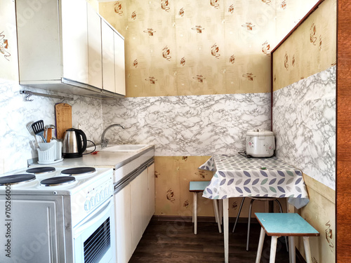 The interior is a small old kitchen with a table, stool, cabinets, sink and stove. Design in the Soviet poor outdated style photo