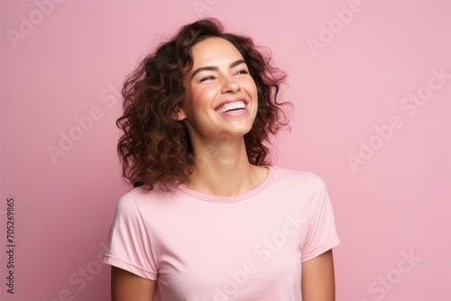 Portrait of a beautiful young woman with curly hair laughing against pink background