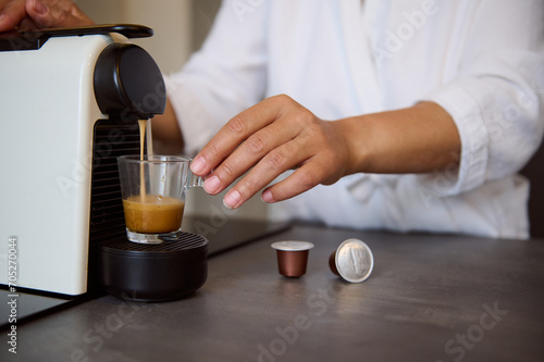 Close-up hands of housewife using a capsule coffee machine preparing freshly brewed espresso coffee in cozy home kitchen photo