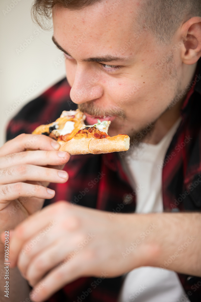 A young man eating a slice of pizza with cheese and tomato sauce. A young man eating a slice of pizza with cheese and tomato sauce.