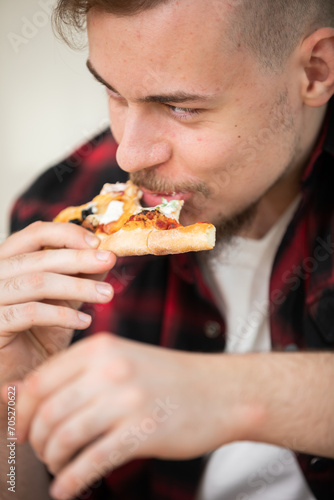 A young man eating a slice of pizza with cheese and tomato sauce.