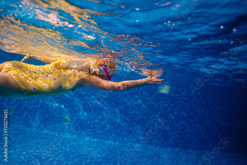 Little child swims underwater in swimming pool, happy active dives and has fun under water, kid fitness and sport 