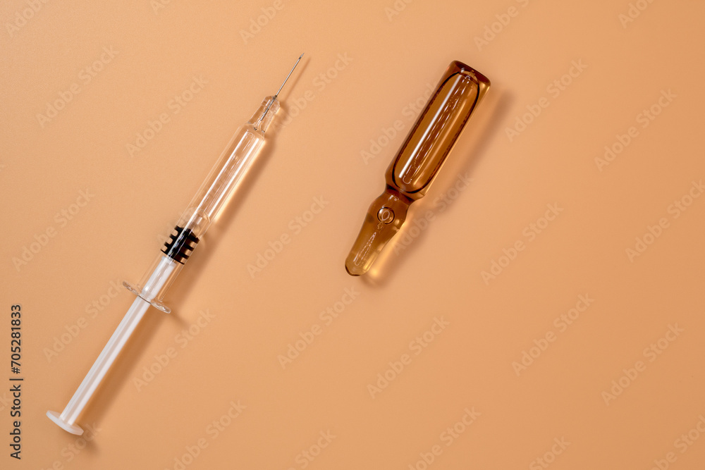Small full syringe with needle on peach background. Next to it is the vial of medicinal liquid (small brown ampoules). Copy Space. Small full syringe with needle on peach background. Next to it is the vial of medicinal liquid (small brown ampoules). Copy Space.