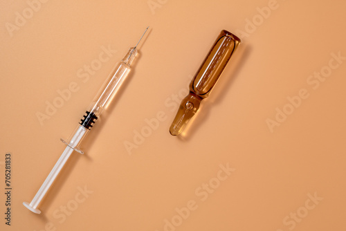 Small full syringe with needle on peach background. Next to it is the vial of medicinal liquid (small brown ampoules). Copy Space.
