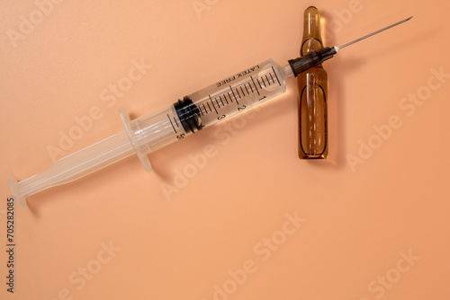 Full 5ml syringe with needle on peach background. Next to it is the vial of medicinal liquid. Copy Space. photo