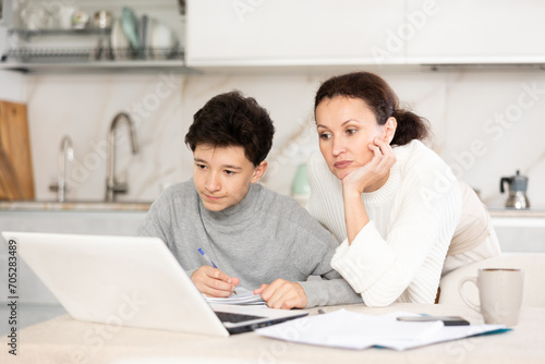 Boy studiyng using laptop, mother helping and explaining