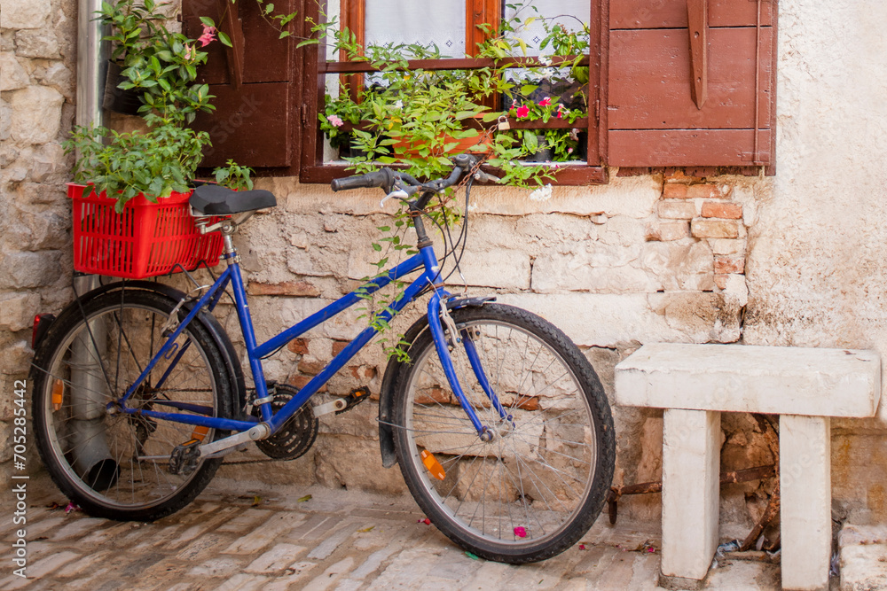 bicycle with a basket near a wall with a window with open shutters and red fresh homemade flowers in pots