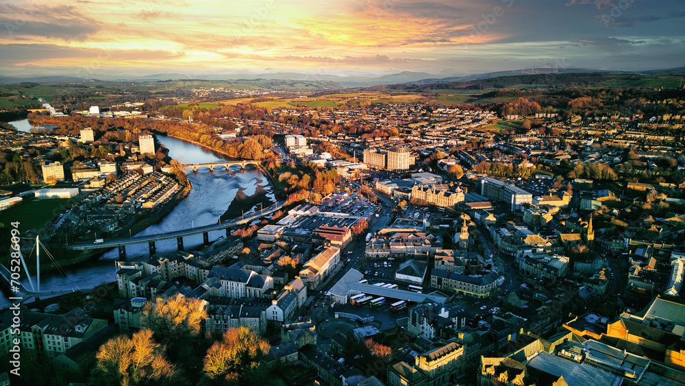 Aerial view of a city Lancaster at sunset with warm lighting, showcasing the urban landscape, buildings, and a river flowing through the center.