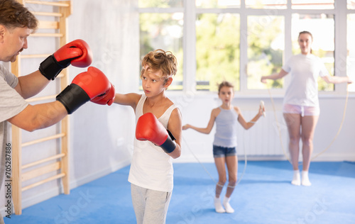 Focused determined preteen boy practicing boxing punches in sparring with father during training in gym. Sports family concept ..