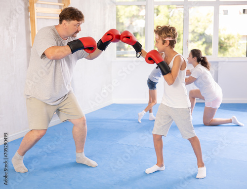 Focused determined preteen boy practicing boxing punches in sparring with father during training in gym. Sports family concept ..