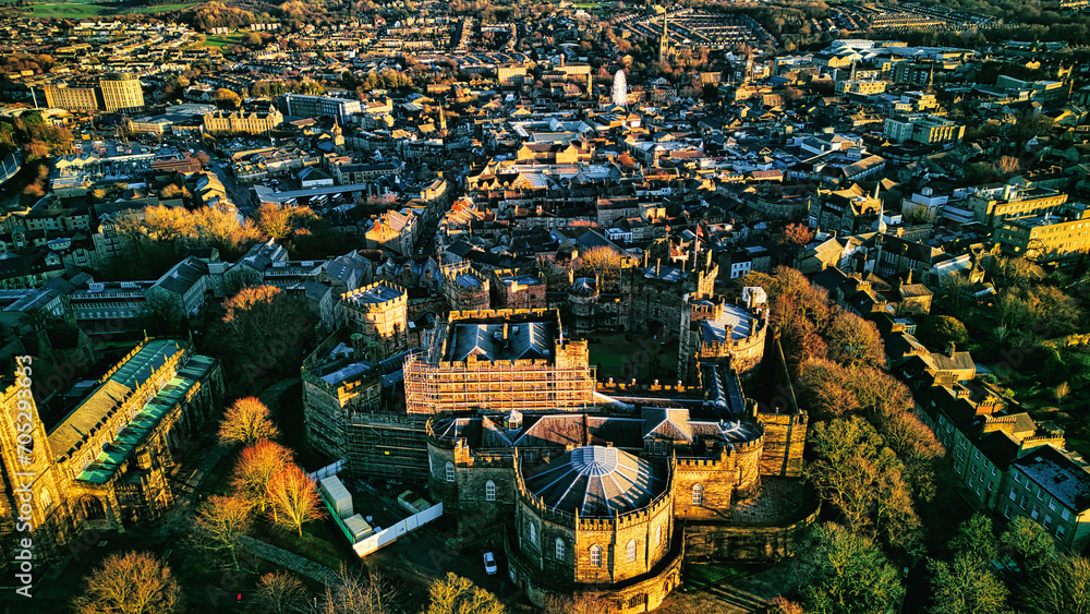 Aerial view of a historic city Lancaster at sunset with warm lighting highlighting architectural details and dense urban landscape.