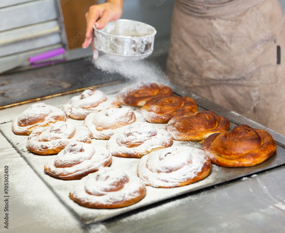 Baker hands dusting freshly baked ensaimadas with powdered sugar in
