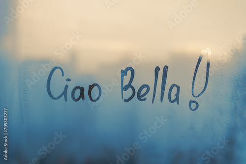 Handwritten text Ciao Bella in Italian language is Bye hi pretty in english on muddy glass wet blue window sunset photo