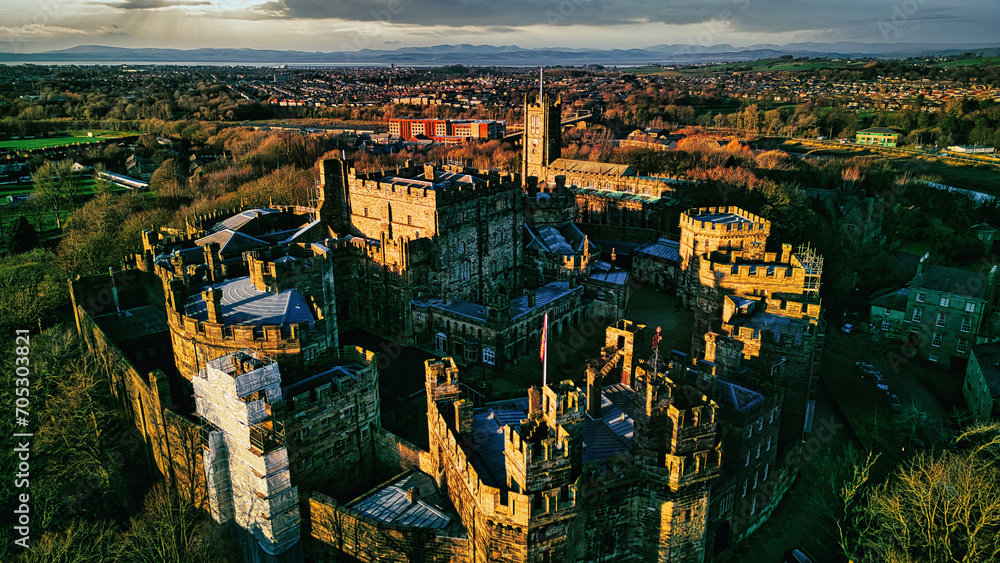 Aerial view of an ancient castle in Lancaster at sunset with lush greenery and a town in the background.