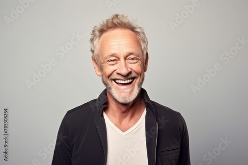 Portrait of a happy senior man laughing while standing against grey background.