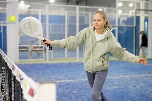 Teenage girl serving ball while playing padel in court during training.