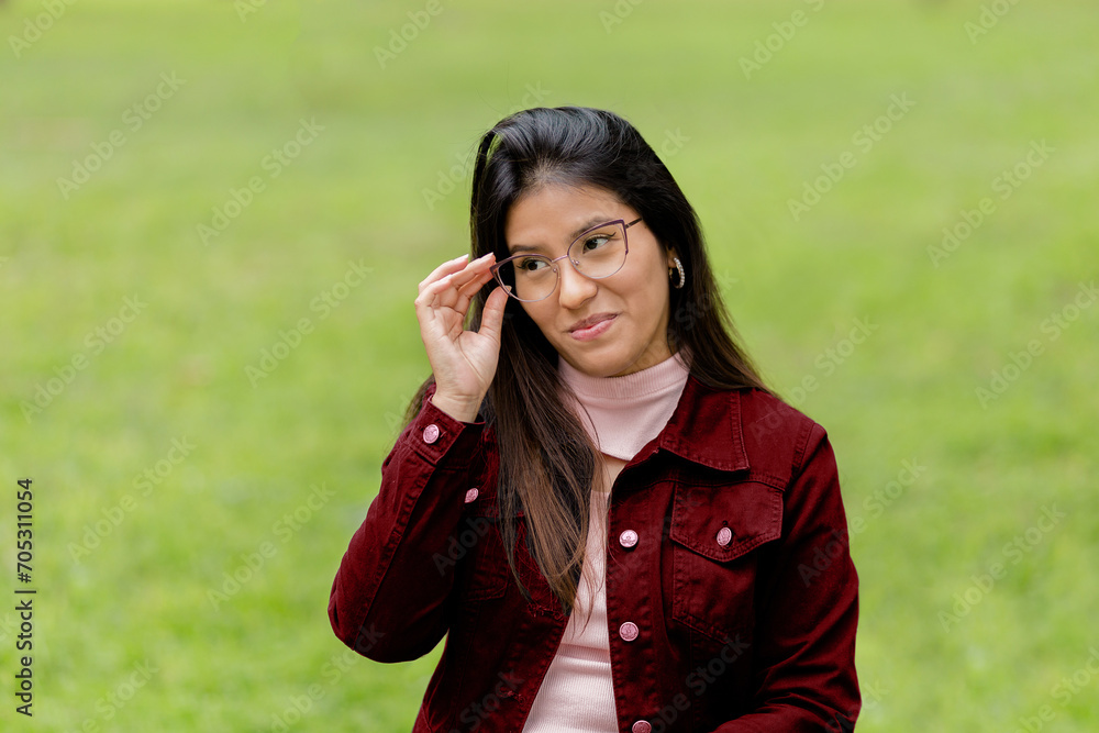 Close-up portrait of a young and beautiful woman with glasses, looking suspiciously at the camera against a green pasque background. Concept of human emotions, facial expression, advertising Close-up portrait of a young and beautiful woman with glasses, looking suspiciously at the camera against a green pasque background. Concept of human emotions, facial expression, advertising