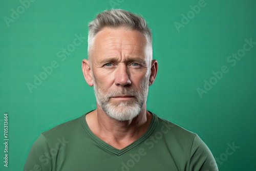 Portrait of senior man with grey hair and beard on green background © Inigo