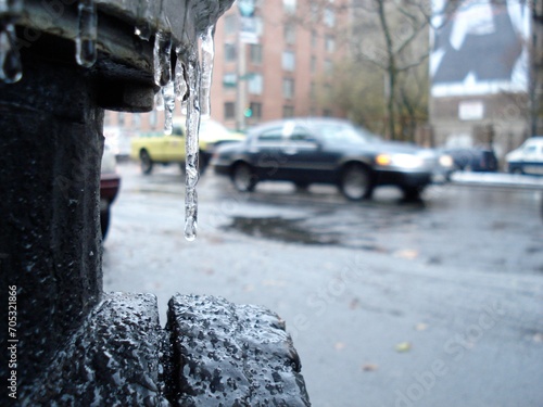 Close up of a black fire hydrant covered with ice with an out of focus car in the background in New York City