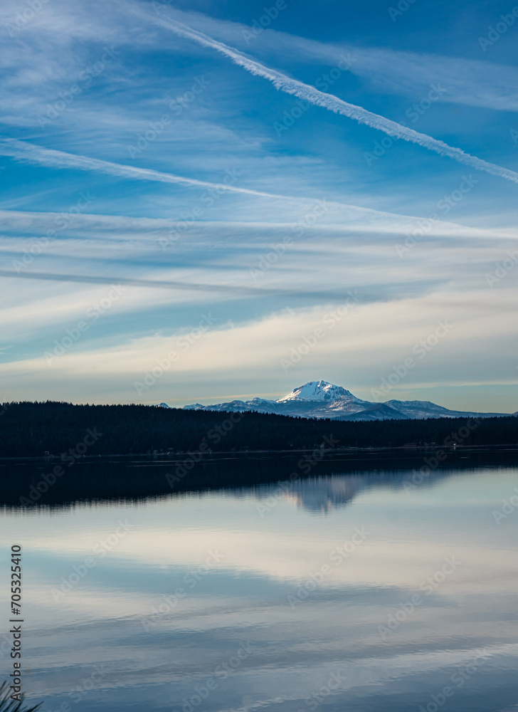 Dramatic image of mount Lassen reflecting in lake Almanor in Northern California with clear calm waters and cloudy skies.