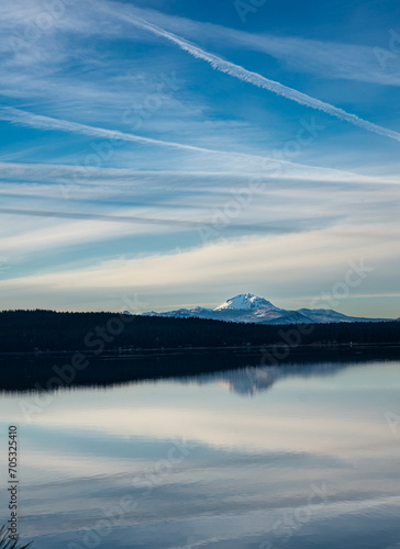 Dramatic image of mount Lassen reflecting in lake Almanor in Northern California with clear calm waters and cloudy skies.