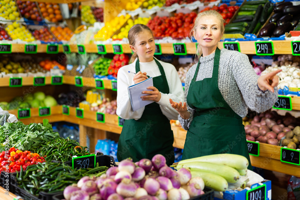 Obraz premium Young girl trainee writes in notebook the order of work in a grocery store