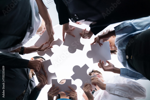 Below view of diverse corporate officer workers collaborate in office connecting puzzle pieces as partnership and teamwork concept. Unity and synergy in business idea by merging jigsaw puzzle. Concord photo