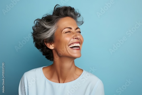 Cheerful mature woman laughing and looking at copy space against blue background