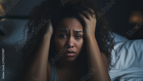 Young woman sitting on bed and holding her head in her hands photo