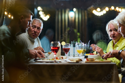 A group of family friends  comprising a young grandson and older individuals  share a delightful dinner in a modern restaurant  exemplifying the concept of healthy aging through intergenerational