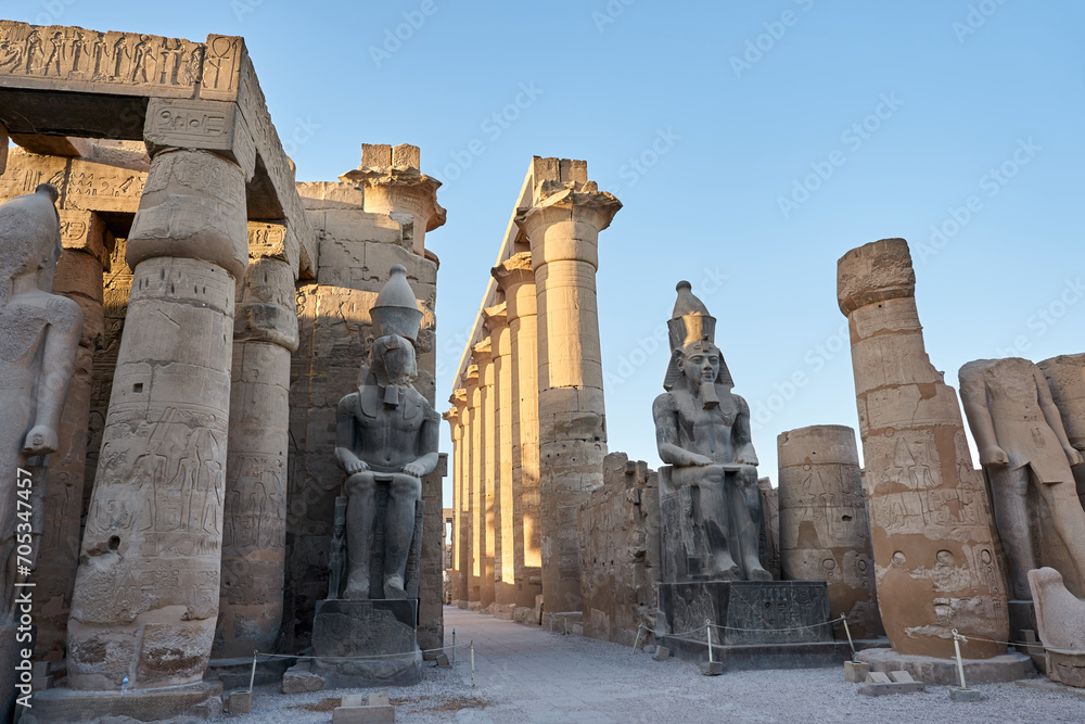 Seated statue of Ramesses II by the First pylon of the Luxor Temple, Egypt. Columns and statues of the Luxor temple main entrance, first pylon, Egypt Seated statue of Ramesses II by the First pylon of the Luxor Temple, Egypt. Columns and statues of the Luxor temple main entrance, first pylon, Egypt