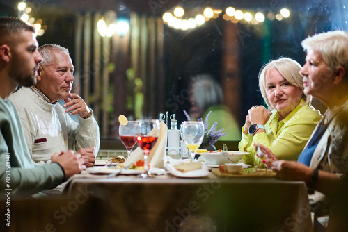 A group of family friends  comprising a young grandson and older individuals  share a delightful dinner in a modern restaurant  exemplifying the concept of healthy aging through intergenerational