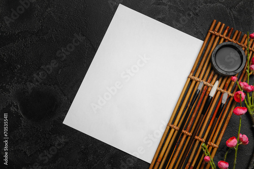 Photography Composition with blank sheet of paper, bamboo mat, brushes and ink on dark background