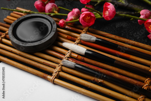 Bamboo mat with brushes, ink and blooming branch on dark background, closeup. International Haiku Poetry Day