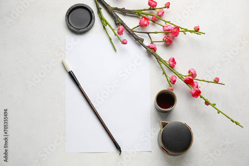 Composition with blank sheet of paper, ink, brush and blooming branch on light background. International Haiku Poetry Day