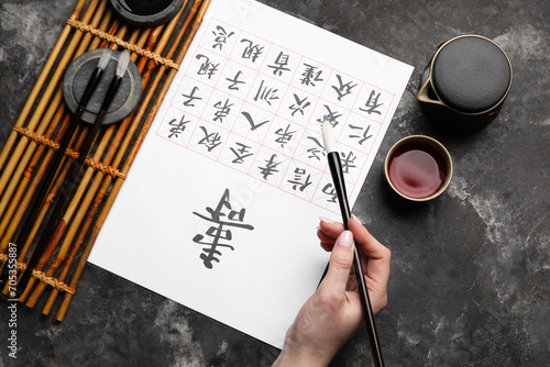Εκτύπωση καμβά Female hand with Asian hieroglyphs, brushes and cup of tea on grunge background, closeup